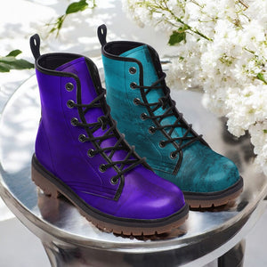 A pair of purple and blue boots are displayed on a silver stand, with white flowers in the background.