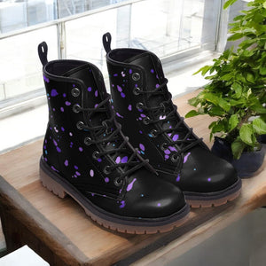 A pair of black boots with purple splatter designs on them, placed on a wooden surface next to a potted plant.