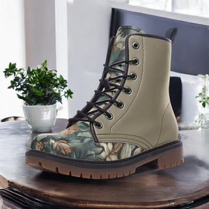 A pair of tan boots with a floral print pattern, placed on a wooden surface next to a potted plant.
