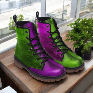 A pair of colorful, patterned boots with green and purple hues are displayed on a wooden surface, with a potted plant visible in the background.