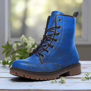 A blue, rugged-looking boot with a lace-up closure and a chunky sole is displayed on a wooden surface, with white flowers in the background.