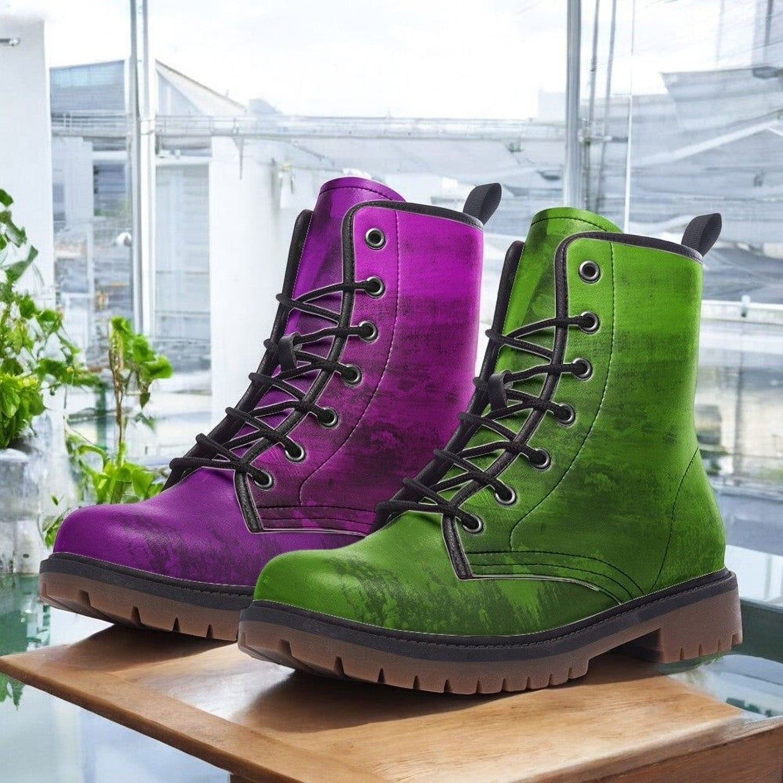 A pair of colorful boots, one purple and one green, are displayed on a wooden surface.