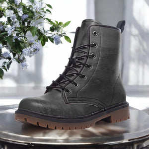 A pair of black leather boots with a rugged sole and lace-up design, placed on a round table with a plant in the background.