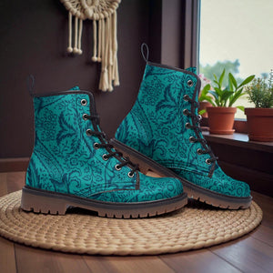 A pair of teal patterned boots with black laces and soles, placed on a woven mat in front of a window with potted plants.