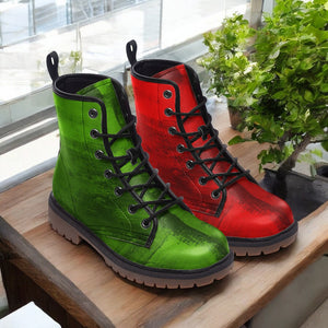 A pair of green and red combat boots are displayed on a wooden surface, with a potted plant visible in the background.