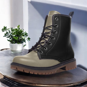 A black and tan leather boot is displayed on a wooden surface, with a small potted plant in the background.