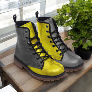 A pair of yellow and gray combat boots are displayed on a wooden surface, with a potted plant visible in the background.
