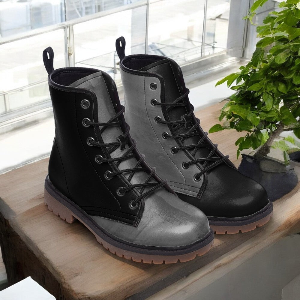 A pair of black and gray combat boots are displayed on a wooden surface, with a potted plant visible in the background.