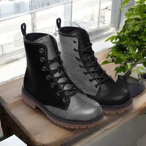 A pair of black and gray combat boots are displayed on a wooden surface, with a potted plant visible in the background.