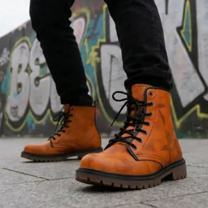 A person wearing black pants and orange boots stands in front of a graffiti-covered wall.