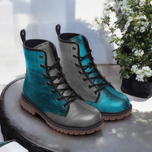 A pair of blue and gray combat boots with black laces and soles, placed on a table next to a potted plant with white flowers.