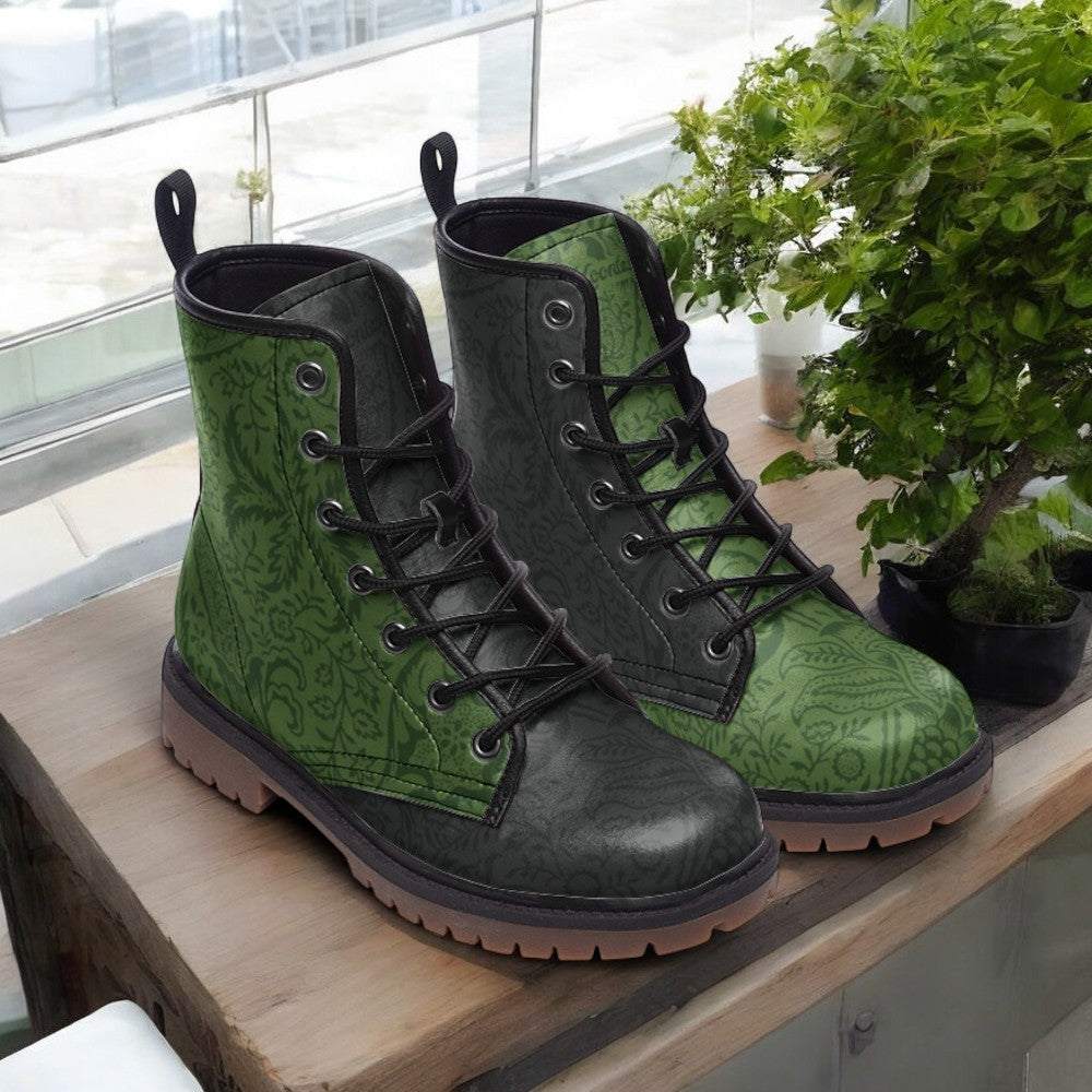 A pair of green patterned boots with black laces and soles, placed on a wooden surface next to a potted plant.