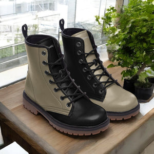 A pair of black and tan boots are displayed on a wooden surface, with a potted plant visible in the background.