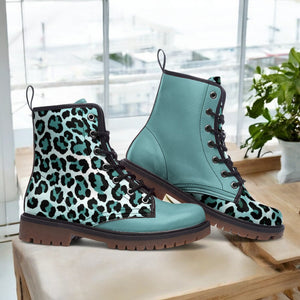 A pair of blue leopard print boots with black laces, placed on a wooden surface near a window.